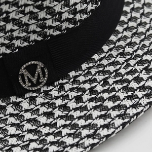 Close-up of black and white woven straw hat featuring a crystal M metal buckle
