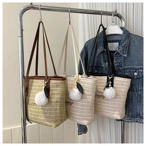 Three straw tote bags in khaki, cream, and black hanging on a rack with pom-pom charms