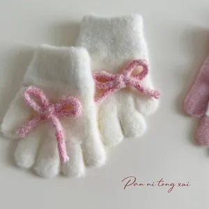 Close-up of soft plush knit gloves in cream with decorative pink bows for girls