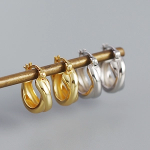 Detail view of gold and silver S925 sterling silver crossover hoop earrings on a metal rod
