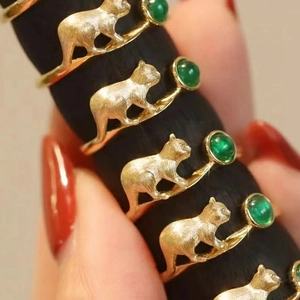 Close-up of matte gold cat rings with round green emerald gemstones on model fingers