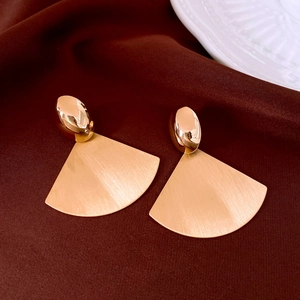 Close-up of golden fan-shaped earrings with brushed metal texture on velvet background