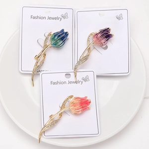 Detailed top view of three enamel tulip brooches with rhinestones on a white plate