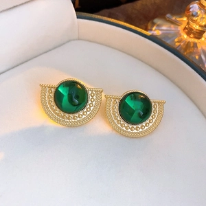 Macro shot of vintage gold earrings with green gemstones on white jewelry cushion