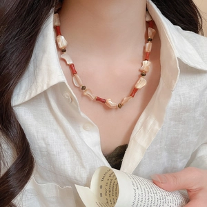 Close-up of beaded necklace with mother of pearl shells and red accents on model