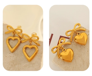 Macro detail of gold bow and heart drop earrings on a minimalist stone background