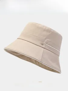 Detail eines beigen Fischerhutes mit strukturiertem Stoff und metallischem M-Logo