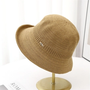 Minimalist camel knit bucket hat for women on a gold stand with metal brand badge
