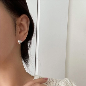Close-up of sparkling heart-shaped zircon stud earrings in silver on female model ear