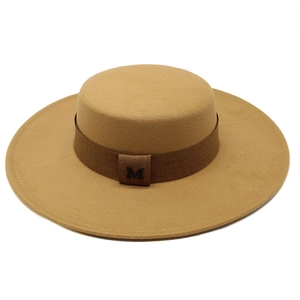 Detail of camel wool boater hat featuring a brown ribbon and a metal M emblem