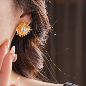 Macro view of a gold floral stud earring with clear zircon inlay worn by a female model