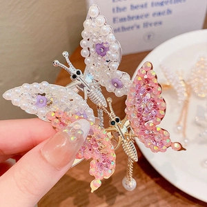 Detailed close-up of a golden butterfly hair clip with rhinestones and pearl tassels