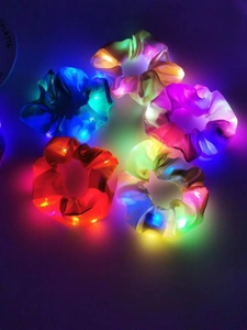 Detail of five luminous LED satin scrunchies glowing in blue green orange yellow and pink