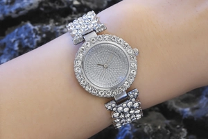 Close-up of a silver rhinestone-studded luxury watch worn on a wrist against a stone background
