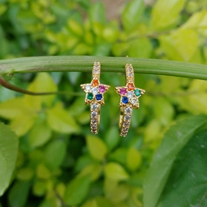 Star-shaped gold earrings with colorful cubic zirconia stones on green nature background