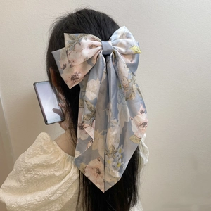 Detail of floral satin bow hair clip with long streamers on light blue fabric