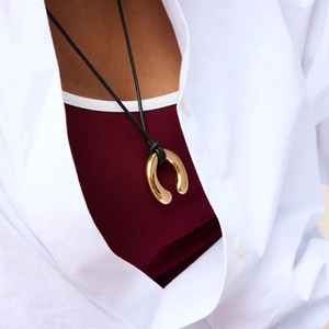 Close-up of golden horseshoe pendant with black cord on a woman wearing white shirt