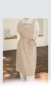 Detail of beige cotton apron featuring pleated waist design and artistic cross back straps