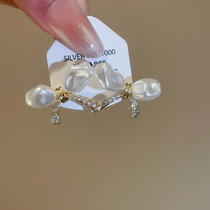 Close-up of gold plated silver earrings with baroque pearls and zircon bow detail