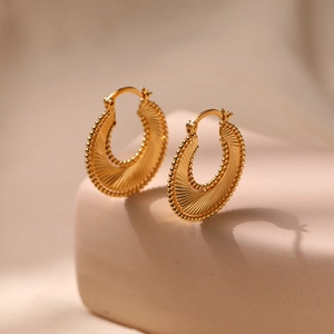 Retro golden spiral hoop earrings with scalloped texture and beaded edges in a warm studio light