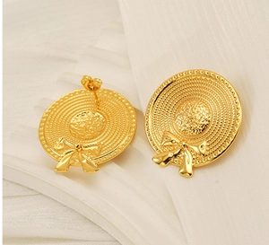 Macro shot of gold sun hat stud earrings with bow details and fine woven texture