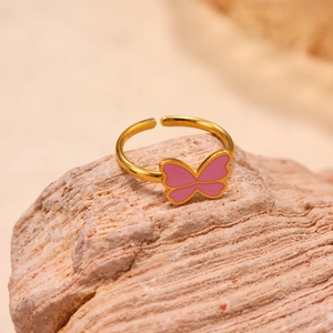 Golden stainless steel butterfly open ring with pink enamel on a natural textured stone