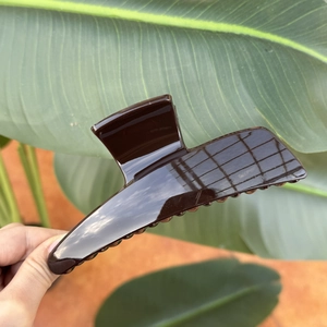 Detail of dark brown oversized glossy hair claw clip held against tropical green leaves