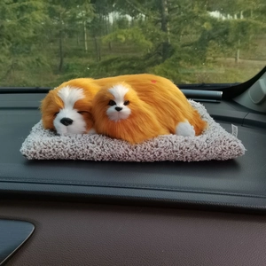 Realistic orange plush puppies on a gray mat displayed on a car dashboard interior