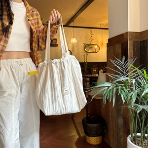 Close-up of white pleated tote bag with woven label in a stylish cafe setting