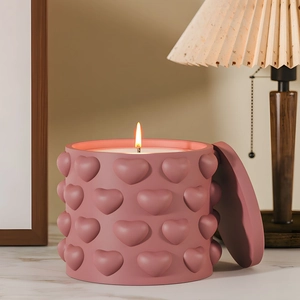 Pink heart embossed scented candle with lid lit on marble countertop in warm home setting