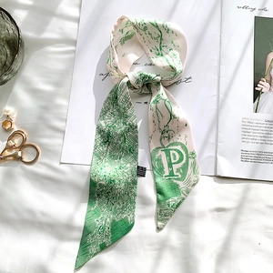 Detail view of satin silk scarf with green floral print and letter P on a magazine