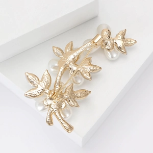 Detailed close-up of the golden leaf brooch back with pin clasp and white pearls