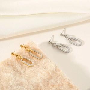 Detail of gold and silver oval drop earrings with micro-pave crystals on stone background