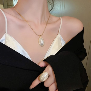 Gros plan du collier de perles ovales plaqué or et de la bague assortie sur le modèle