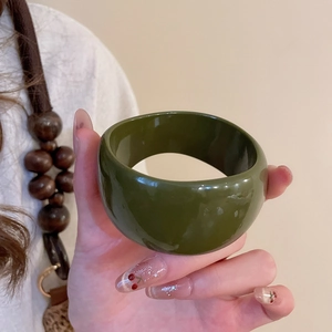 Close-up of a wide dark green resin bangle with smooth polished mirror finish surface