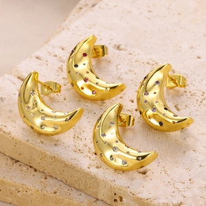 Macro view of gold moon earrings with colorful zircon stones on textured beige stone