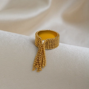 Detail view of a golden tassel bead ring resting on a textured white linen fabric