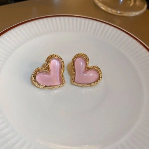 Detail of pink heart-shaped earrings with gold textured edges on a ceramic plate