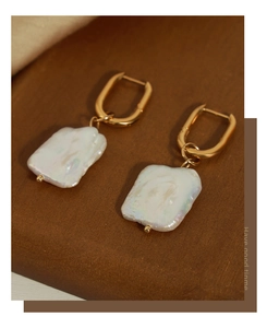 Detailed view of baroque pearls on gold hoop earrings over a dark wood background