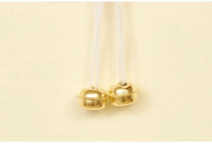 Close-up of dual golden metal Christmas bells with white woven hanging ropes
