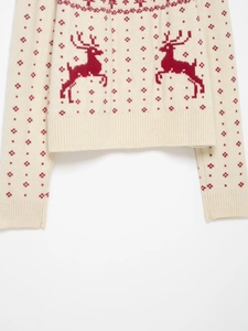 Close-up of ribbed cuffs and hem on cream Christmas sweater with red reindeer patterns