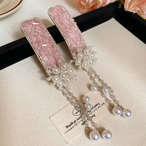 Detailed macro of pink diamond floral hair clips with dangling pearl tassels on a tray