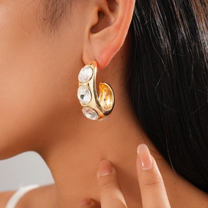 Close-up of gold C-shaped geometric earring with three large crystals on a model