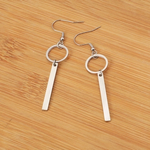 Silver geometric earrings with ring and bar pendants on a rustic wood background