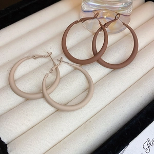 Close-up of matte metal hoop earrings in beige and coffee brown colors on a display box