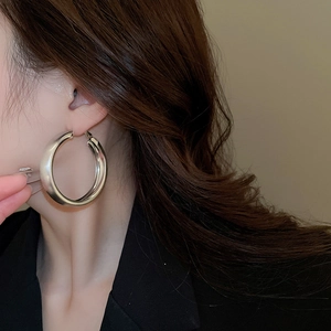 Macro shot of large polished silver hoop earring worn by a model in black blazer