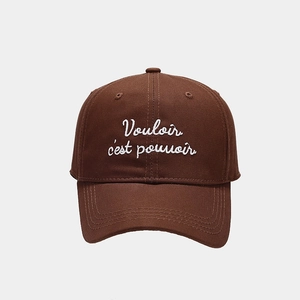 Detail view of white embroidered French quote on a brown cotton baseball cap