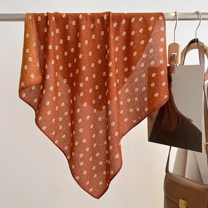 Detail of caramel silk scarf with white leaf pattern hanging on a metal rod
