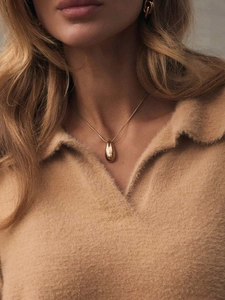 Close-up of golden teardrop pendant necklace worn with a warm beige knit sweater