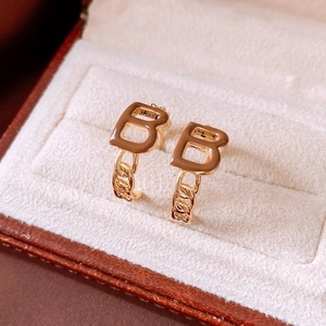 Macro shot of gold-plated B-letter C-shape earrings with chain detail in jewelry box